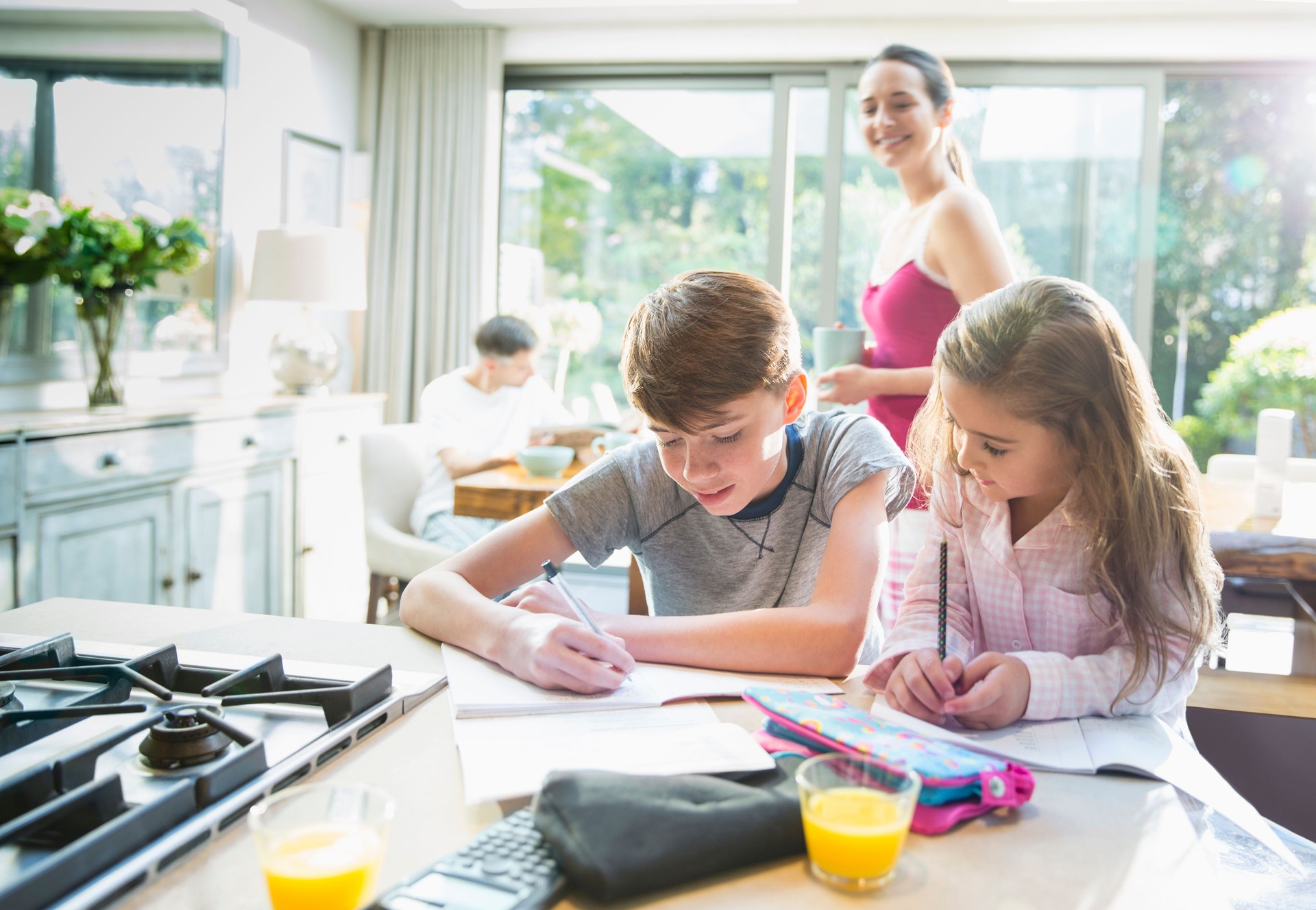 Mother watching brother and sister doing homework at kitchen counter